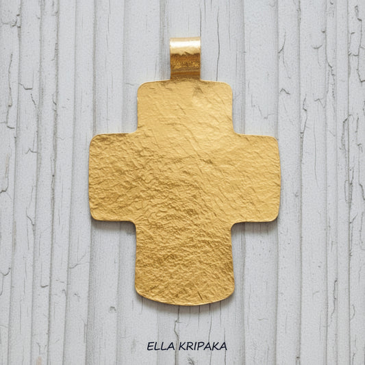 Hammered 24k gold textured cross pendant on a grey rustic wooden surface, artist-jeweler 'Ella Kripaka' branding