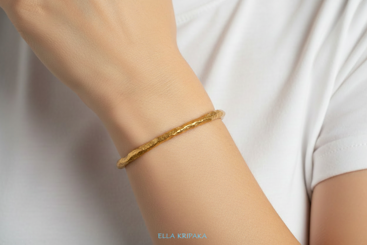 Organic hammered 24k 9999 gold bracelet uneven cuff is worn by a woman and with a white background, branding artist-jeweler name 'Ella Kripaka'