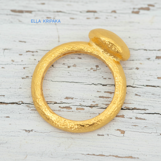 Hammered 24k 9999 Gold ring with convex disk signet Ancient Rome style and with forged textured gold on a white old wooden surface, artist-jeweler's name 'Ella Kripaka' branding