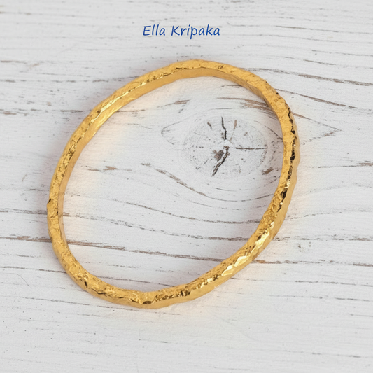 Organic 24k gold textured bangle thick bracelet with uneven edges and on a white wooden background, artist-jeweler name 'Ella Kripaka'