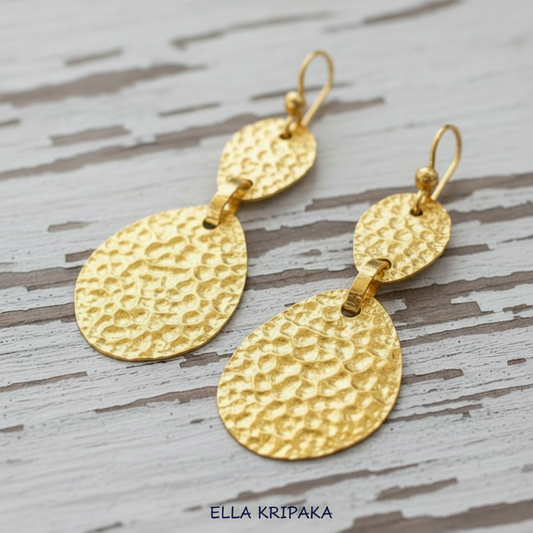 24k gold hammered uneven oval earrings with uneven shapes and textured reliefs, displayed on rustic white wood background, branding name 'ELLA KRIPAKA' is printed at the bottom