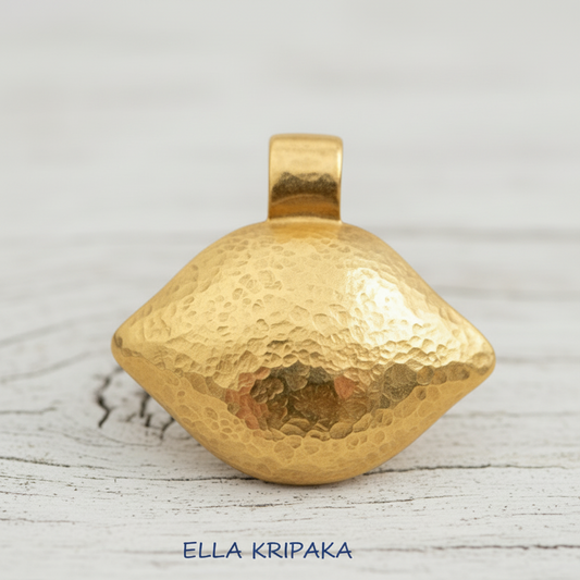 24k gold hammered dome oval pendant with shiny forged textures is on white rustic wooden surface, artist's name 'Ella Kripaka'