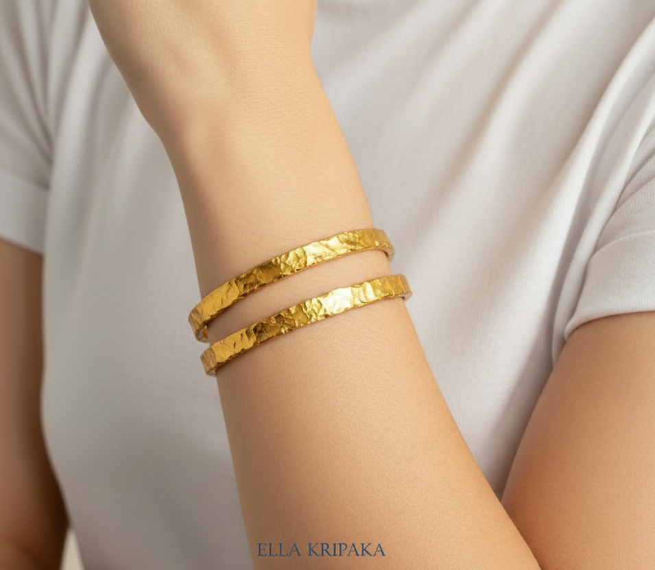 Organic hammered 24k 9999 Gold two bangles uneven bracelets worn by a person on wrist and with white t-shirt background, artist's name 'Ella Kripaka' branding
