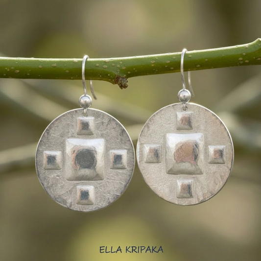 Hammered 24k 9999 Hammered 24k Gold disk earrings with five convex squares are hanging on a branch with 'Ella Kripaka' branding