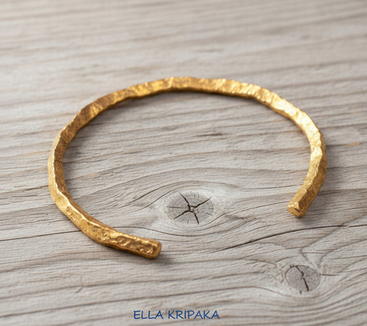Organic hammered 24k 9999 gold bracelet uneven cuff on a old wooden background, branding artist-jeweler name 'Ella Kripaka'