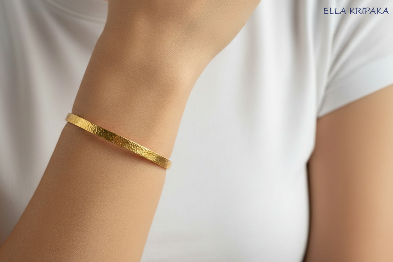 Hammered 22k gold bangle bracelet Ancient Rome style on on model's wrist and on white blurred t-shirt background, with 'Ella Kripaka' branding