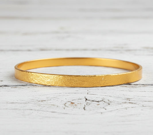 Hammered 22k gold bangle bracelet Ancient Rome style on rustic white wooden surface with 'Ella Kripaka' branding