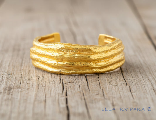 Organic 24k 9999 gold hammered uneven bracelet cuff on old wooden background, indicating it is a custom-made jewelry with creator's name 'Ella Kripaka'