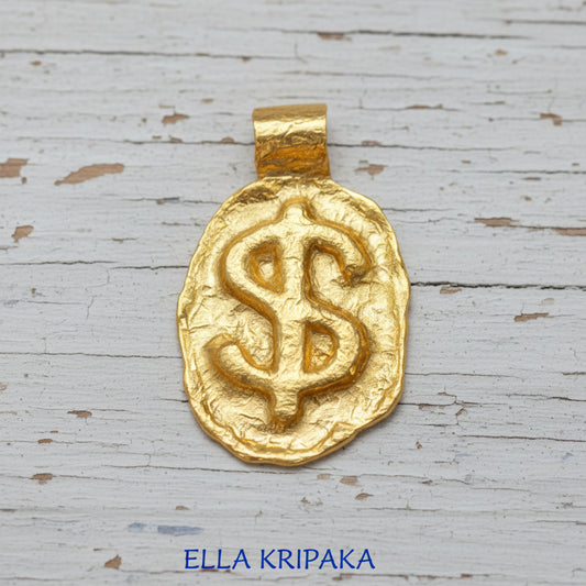 Organic 24k gold hammered pendant with convex sign 'Dollar' and with thick uneven edges on old white wooden surface, branded 'Ella Kripaka'