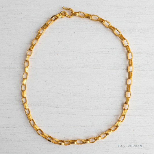 Hammered 24k chain necklace as in Ancient Rome on a white wooden background, branding artist name 'Ella Kripaka'