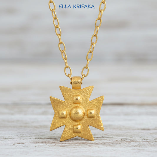 24k gold Byzantine cross pendant textured hammered with convex pattern and with chain on white rustic wooden background, with 'Ella Kripaka' branding