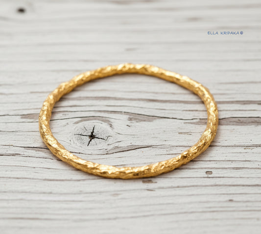 Organic hammered 24k 9999 gold bracelet uneven bangle on a old white wooden background, branding artist-jeweler name 'Ella Kripaka'