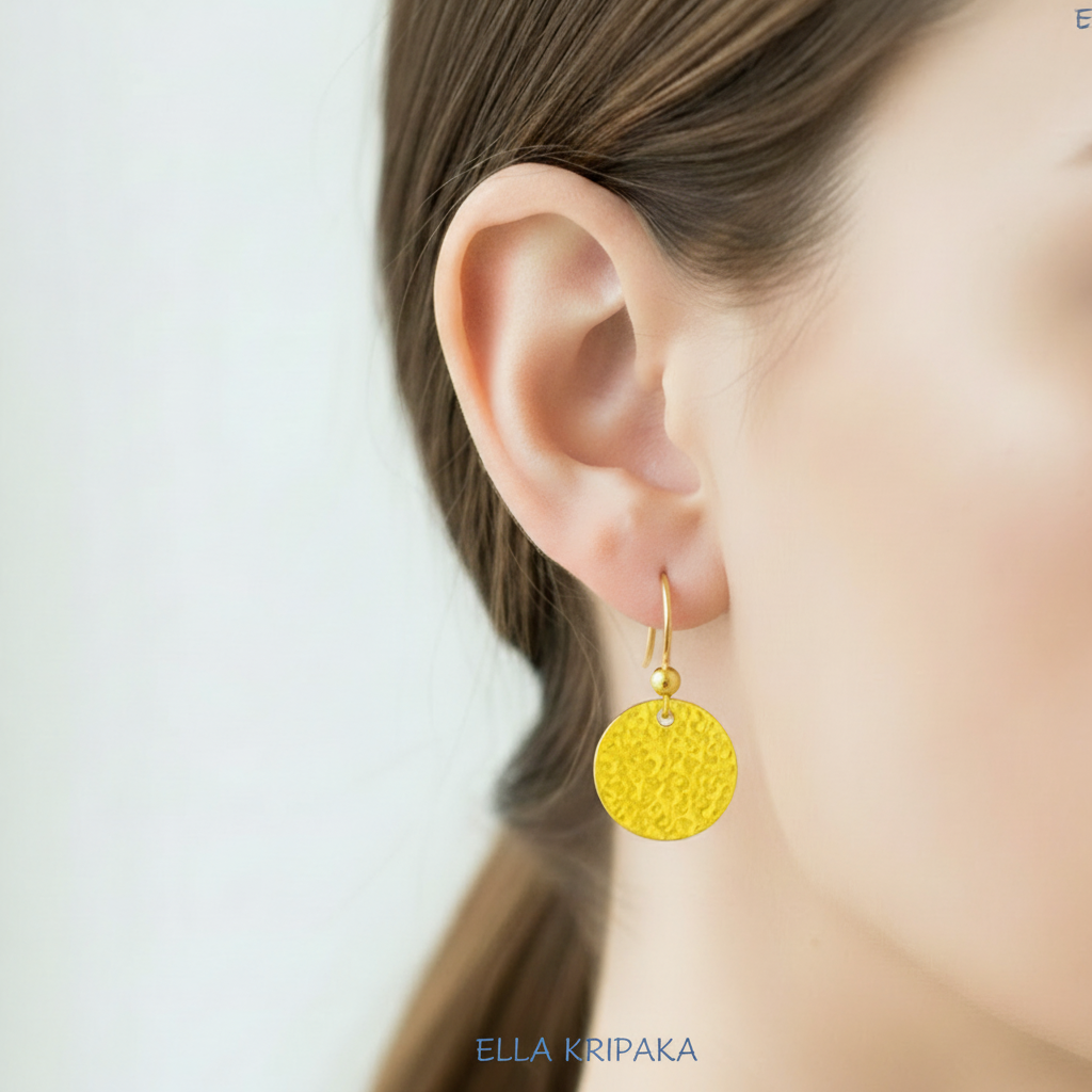 24k 9999 gold hammeted disk earring worn by a person with a blurred background