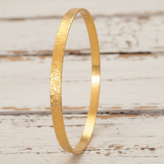 24k 9999 gold hammered Ancient Rome style bracelet bangle on white rustic wooden surface, indicating it is a custom-made jewelry with creator's name 'Ella Kripaka'