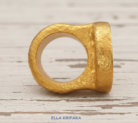 Hammered 24k 9999 Gold thick ring disk signet Ancient Rome style and Byzantine style with a textured gold on a white old wooden background, branded 'Ella Kripaka'