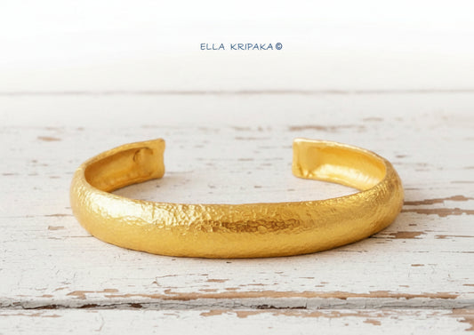 24k 9999 gold hammered Ancient Rome style bracelet cuff on white wooden background, indicating it is a custom-made jewelry with creator's name 'Ella Kripaka'