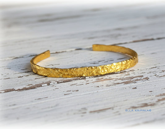 Organic hammered 24k 9999 gold bracelet uneven cuff on a old white wooden background, branding artist-jeweler name 'Ella Kripaka'