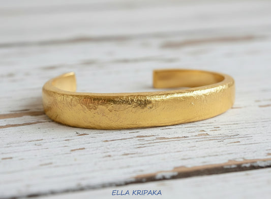 Hammered 24k 9999 Gold thick cuff bracelet Ancient Rome style on a wooden background with 'Ella Kripaka' branding