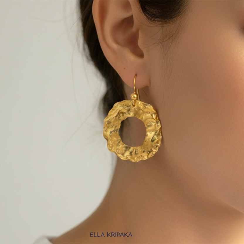 Organic 24k 9999 gold hammered wavy hoops earrings with shiny gold textures worn by a woman and on grey background, artist-jeweler's name 'Ella Kripaka'