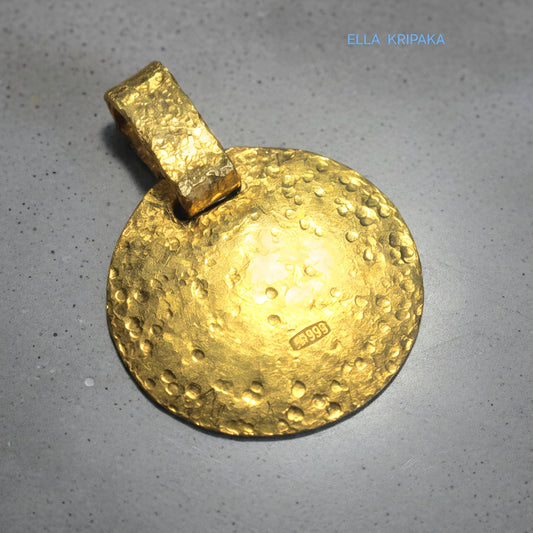 Hammered 24k gold, pure 9999 gold disk pendant with shiny forged gold textures on grey concrete surface, artist-jeweler 'Ella Kripaka' branding