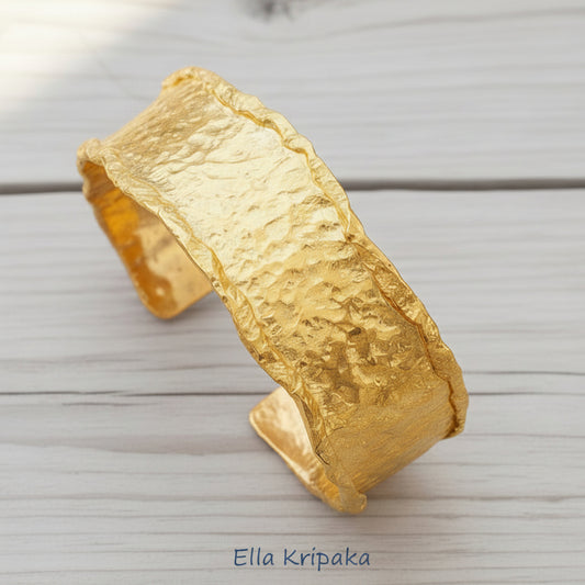 Organic hammered 24k gold bracelet cuff wifh folded uneven edges on a rustic light wooden background, branding artist 'Ella Kripaka'