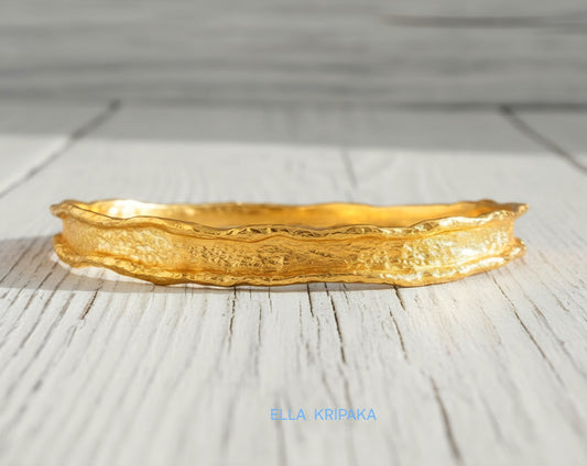 Hammered 22k gold organic textured bangle bracelet with uneven edges on old white wooden surface with 'Ella Kripaka' branding