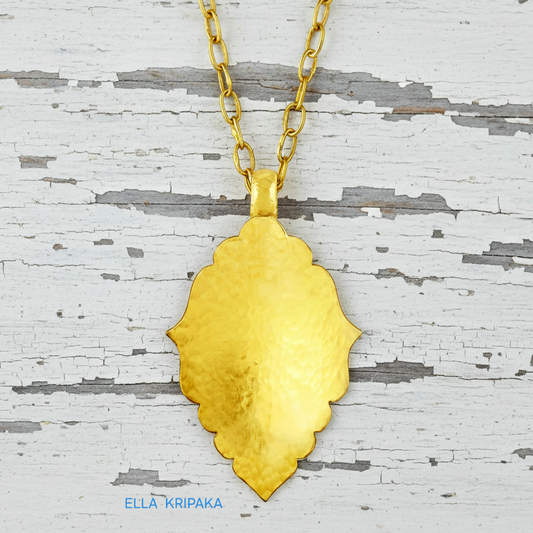 Hammered 24k gold Byzantine ornament pendant with thick chain on a white rustic wooden surface with 'Ella Kripaka' branding