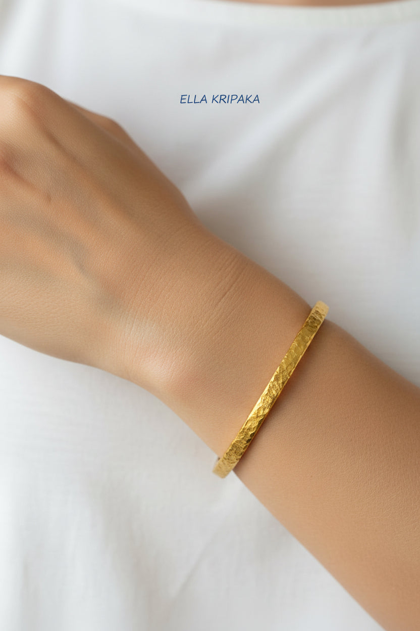 Hammered 24k 9999 gold bangle thick bracelet Ancient Rome style worn by a woman on hand and a white t-shirt background, artist-jeweler name 'Ella Kripaka' branding