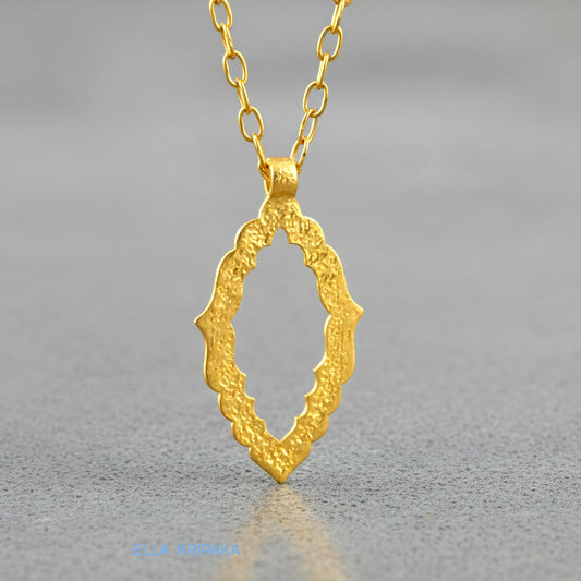 Hammered 24k gold Byzantine ornament pendant wuth a chain on a grey concrete surface with 'Ella Kripaka' branding