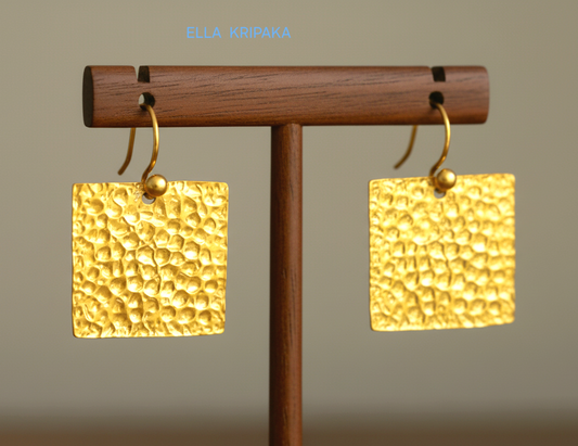 Organic 24k gold hammered textured square earrings on a wooden stand with a neutral background, artist 'Ella Kripaka' branding