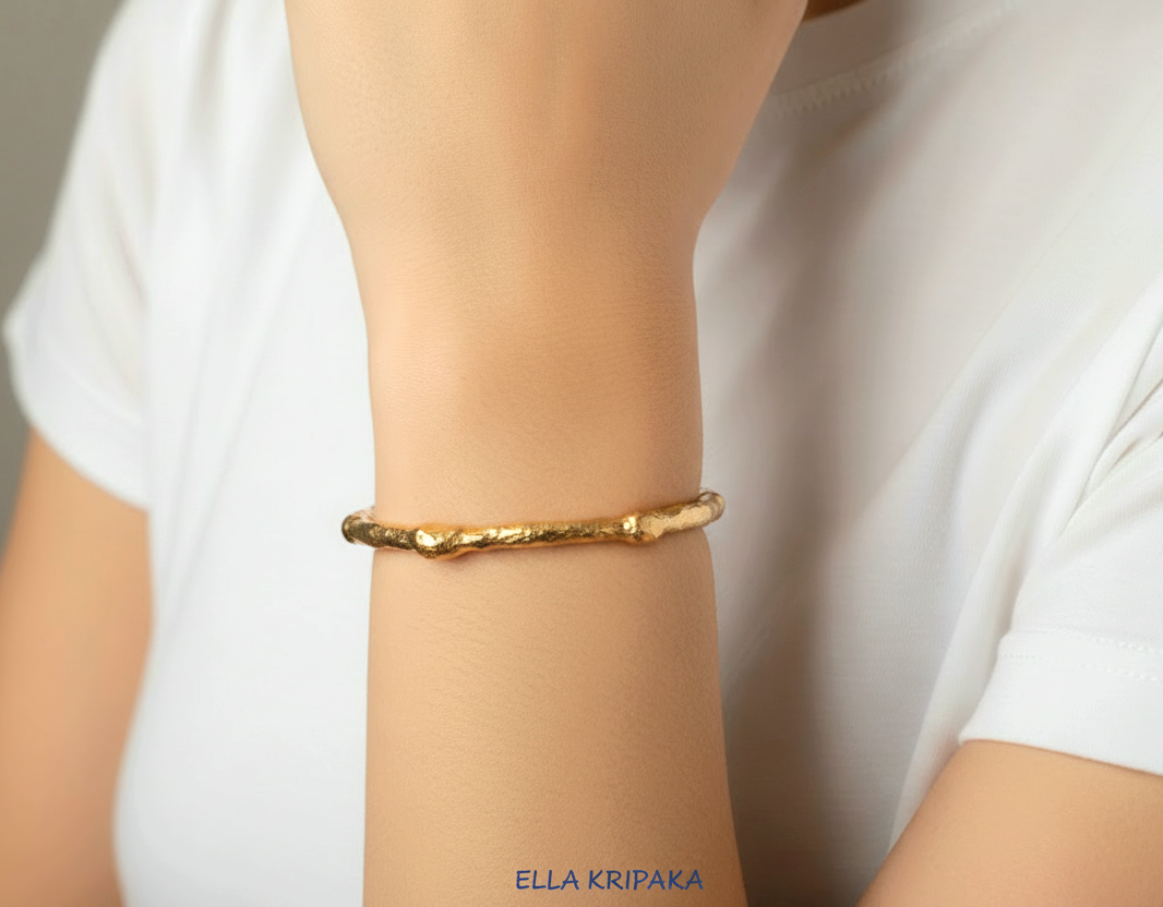 Organic hammered 24k 9999 gold bracelet uneven cuff worn by a person and on a white t-shirt background, branding artist-jeweler name 'Ella Kripaka'