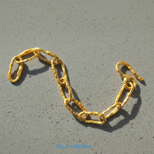 Organic 24k gold large chain bracelet with uneven hammered textures on a grey concrete surface, and with artist 'Ella Kripaka' branding