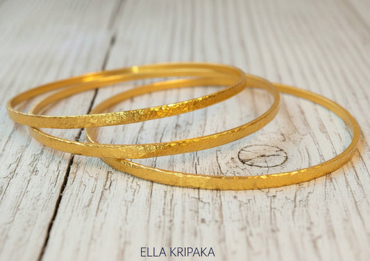 Hammered 22k gold three textured bangles bracelets Ancient Rome style on old wooden surface with 'Ella Kripaka' branding