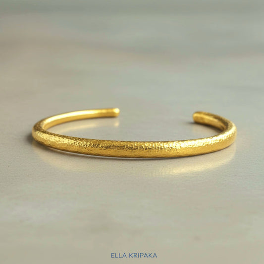 Hammered 24k gold cuff textured bracelet on a grey background, artist-jeweler name 'Ella Kripaka' branding