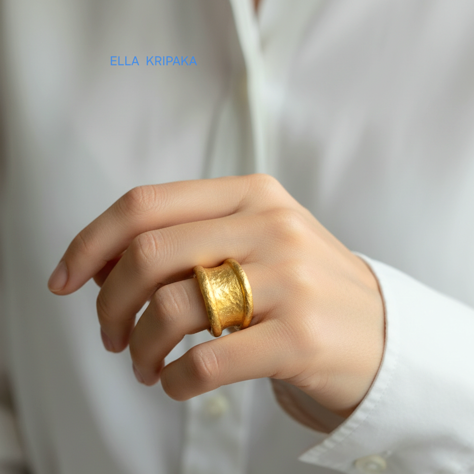 Organic hammered 24k Gold 9999 gold ring signet with thick edges and with textured surface on person's finger on a blurred background, branded 'Ella Kripaka'