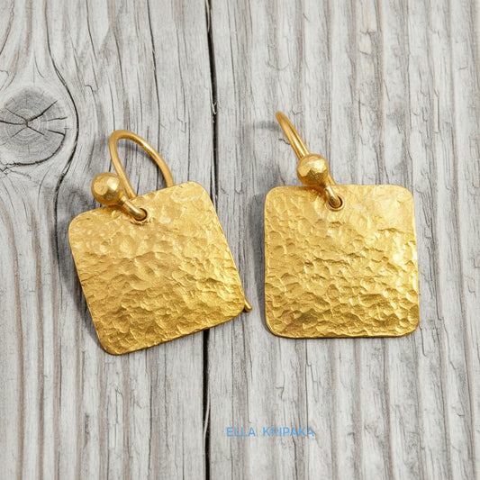 Hammered 24k gold, pure 9999 gold square earrings with shiny forged gold textures on old wooden surface, artist-jeweler 'Ella Kripaka' branding