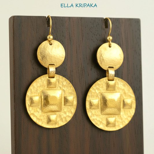 Solid 24k 9999 gold hammered Byzantine earrings with hook clasps and shiny forged gold textures on dark wooden earring stand on grey background, artist's name 'ELLA KRIPAKA'
