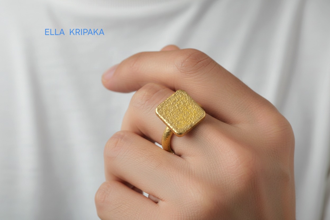 Hammered 24k 9999 Gold thick ring square signet Ancient Rome style with a textured forged gold surface worn by a person on a finger and on a white t-shirt background, branded 'Ella Kripaka'
