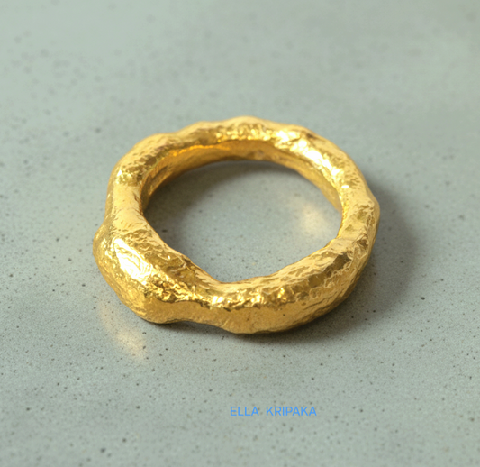 organic hammered 24k Gold thick uneven ring signet with a textured gold reliefs on a grey concrete background, branded 'Ella Kripaka'
