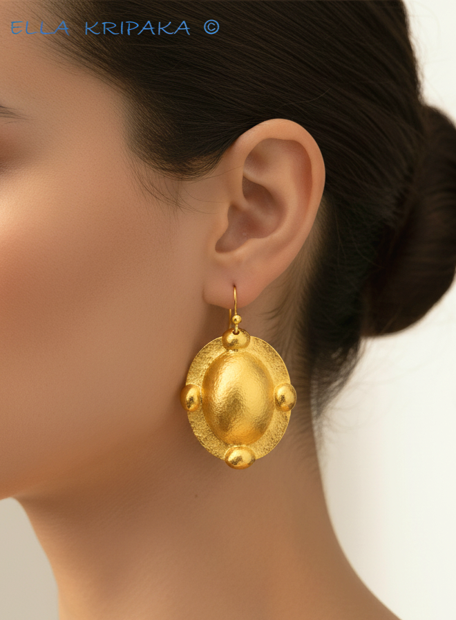 Hammered 24k gold, pure 9999 gold convex ovals Byzantine earring with shiny forged gold textures worn on a woman and with light grey background, artist-jeweler 'Ella Kripaka' branding