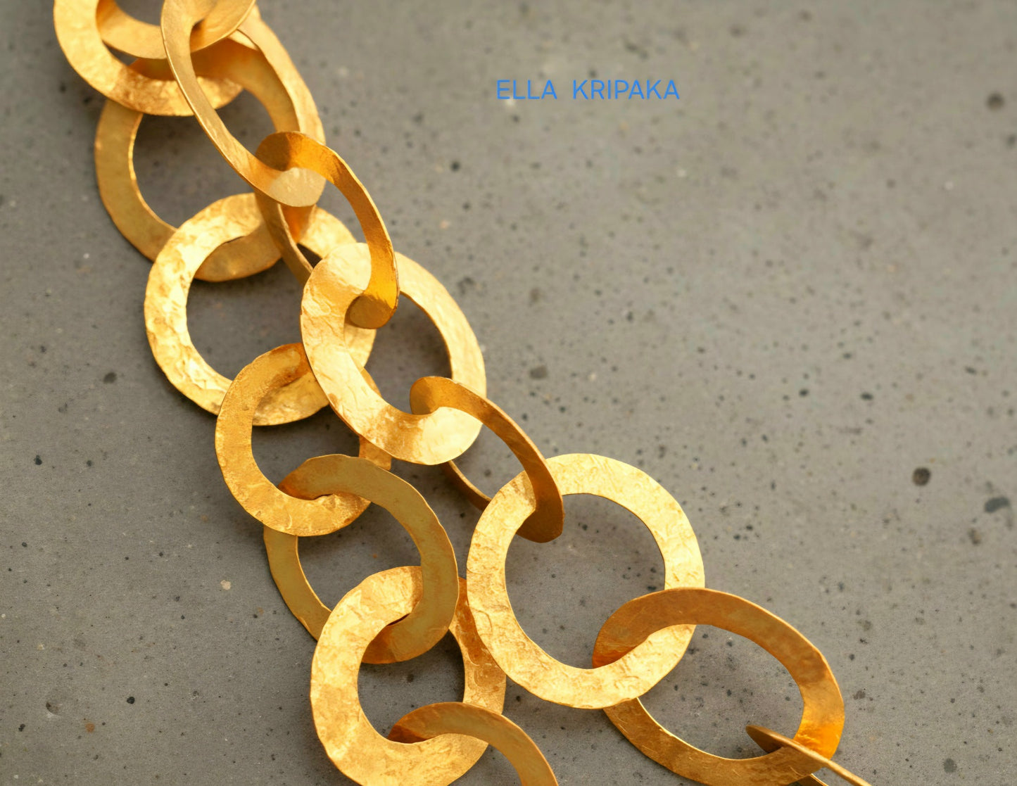 22k gold hammered chain necklace with different links on a grey concrete surface, and with 'Ella Kripaka' branding