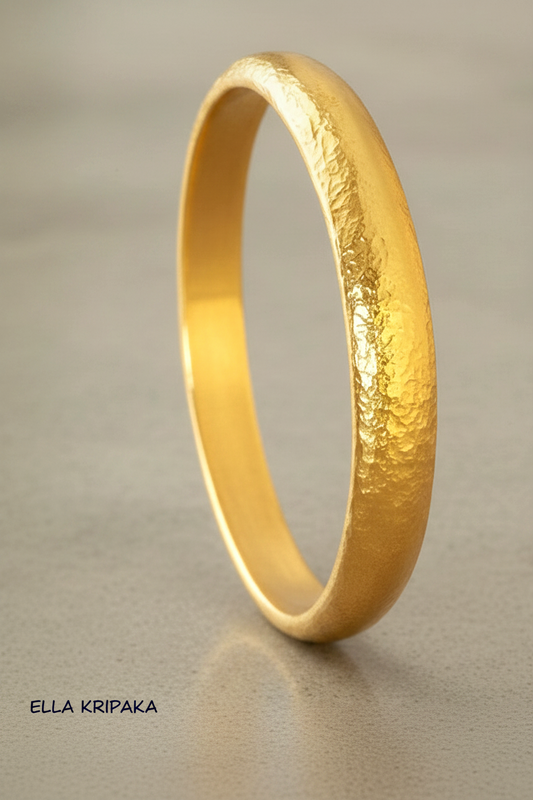 Hammered 24k gold bangle thick bracelet with rounded edges on grey concrete background, artist-jeweler 'Ella Kripaka' branding