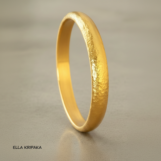 Hammered 24k gold bangle thick bracelet with rounded edges on grey concrete background, artist-jeweler 'Ella Kripaka' branding