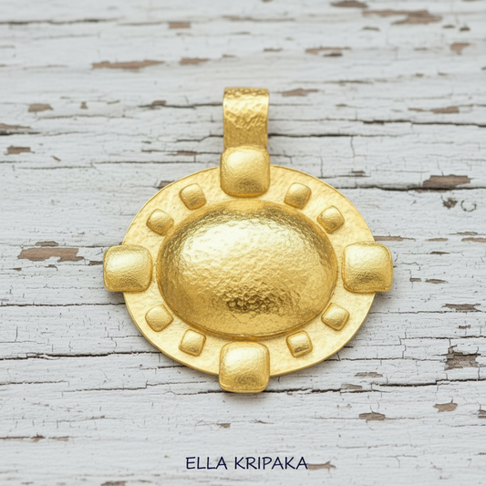Hammered 24k gold Byzantine convex pendant on old wooden surface with 'Ella Kripaka' branding