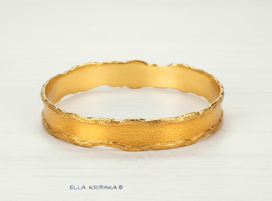 Organic Hammered 24k Gold Bangle Bracelet with uneven thick edges and shiny gold textures on a white wooden surface, branding artist-jeweler 'Ella Kripaka'