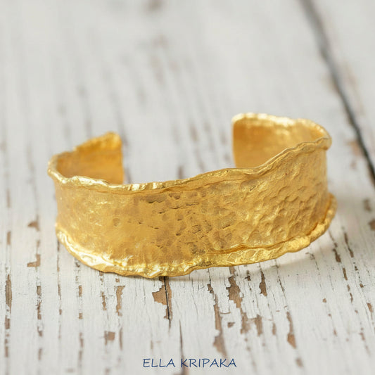 Organic hammered 24k gold bracelet cuff wifh folded uneven edges on a rustic white wooden background, branding artist 'Ella Kripaka