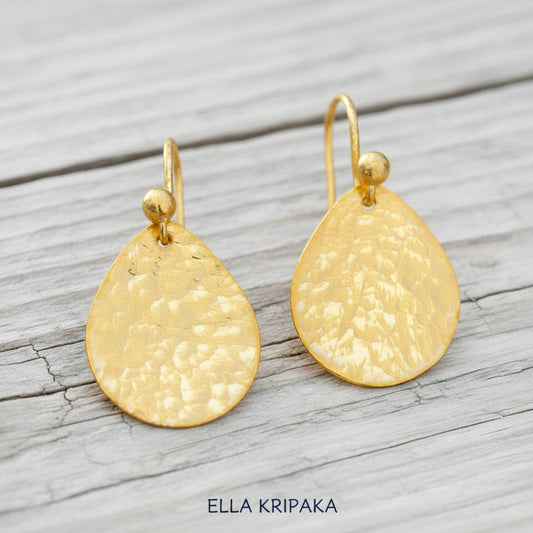 Hammered 24k gold, pure 9999 gold drop earrings with shiny forged gold textures on old wooden surface, artist-jeweler 'Ella Kripaka' branding