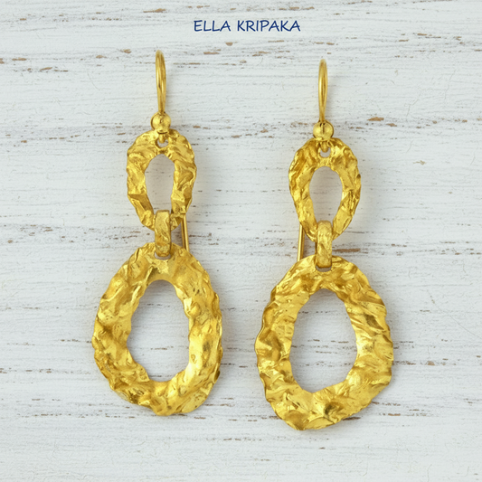 Organic hammered uneven 2 ovals hoops 24k Gold earrings with wavy textures on a white rusic wooden surface, and with 'ELLA KRIPAKA' branding