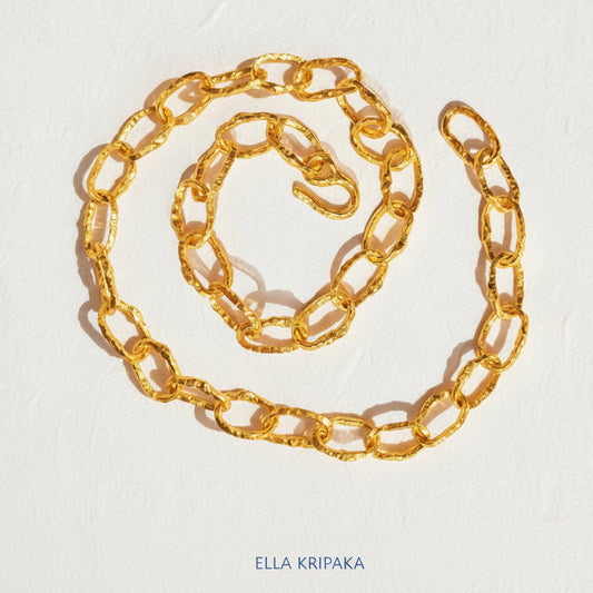 Organic 24k Gold hammered uneven textured chain necklace with thick hook clasp on a white craft paper surface, with artist 'Ella Kripaka' branding