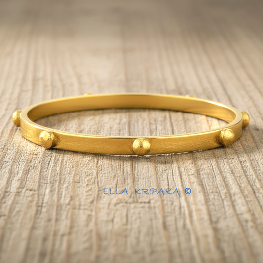 24k gold hammered bangle textured bracelet with convex rounds on light rustic wooden surface, artist 'Ella Kripaka' branding